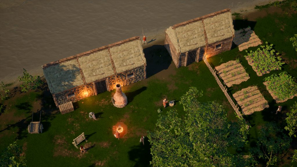 Two thatched log buildings at dusk beside tilled garden rows, a domed clay oven and a firepit burning between them, a handcart and split-rail fencing, settlers at work